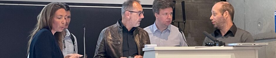 5 personnes au pupitre dans un amphitheatre, la figure de l'une d'entre-elles est cachée.